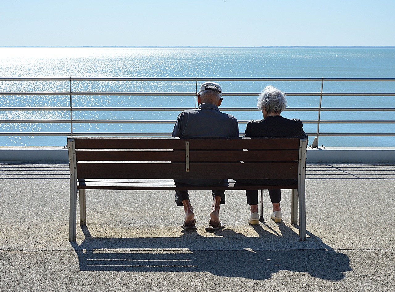 old couple sitting on bench and watching sea
